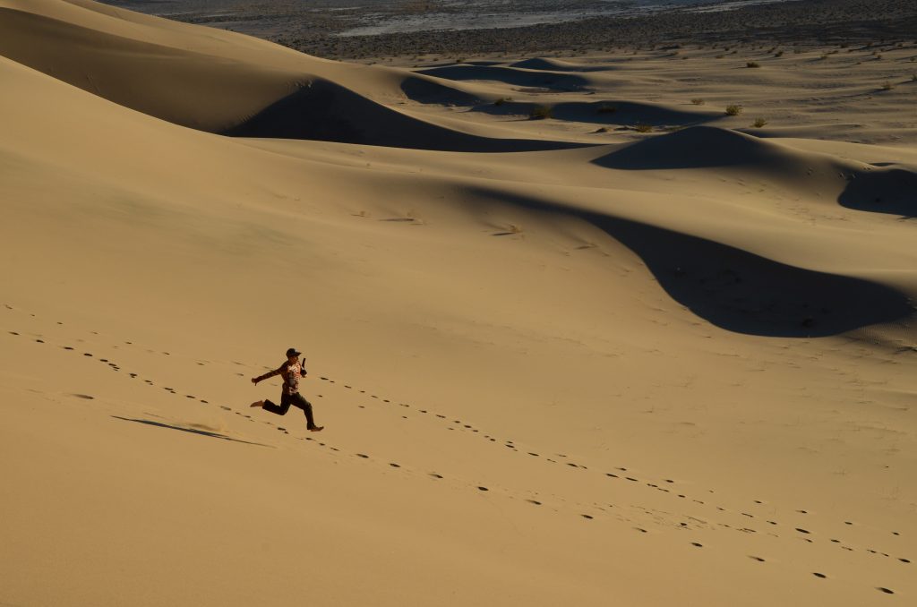 Person running downhill in sand.